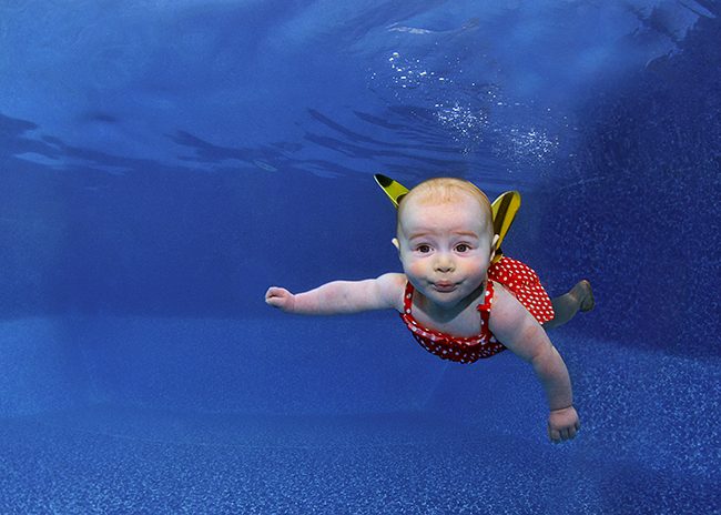 Happy baby swimming just under the surface during a first-water session in Barcelona.
