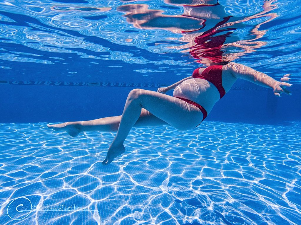 Underwater maternity portrait, pregnancy bump in profile above a sunlit pool floor, Barcelona.